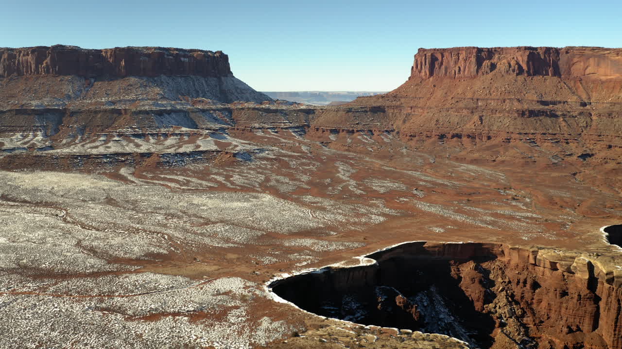 A panoramic view of a vast red rock desert landscape with snow patches