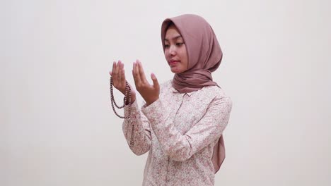 young asian muslim woman standing while praying using prayer beads