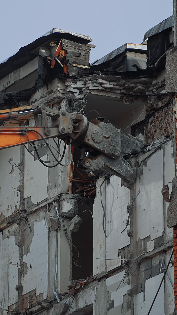Demolishing machine claw tries to grab the concrete block to tear it off. Excavator working at dismantling the ruined house. Vertical video