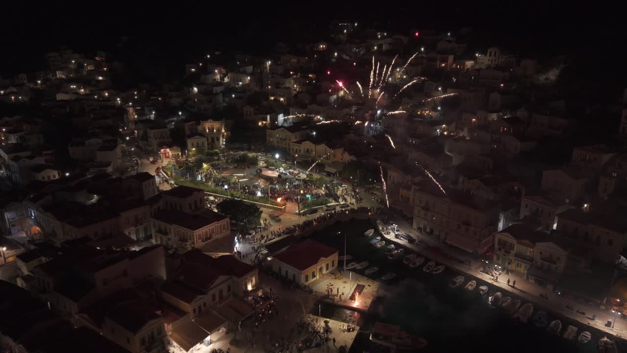 Nighttime drone footage of fireworks celebration in Symi, Greece showing colorful explosions against the dark sky. Filmed with 3x telephoto D-Log M