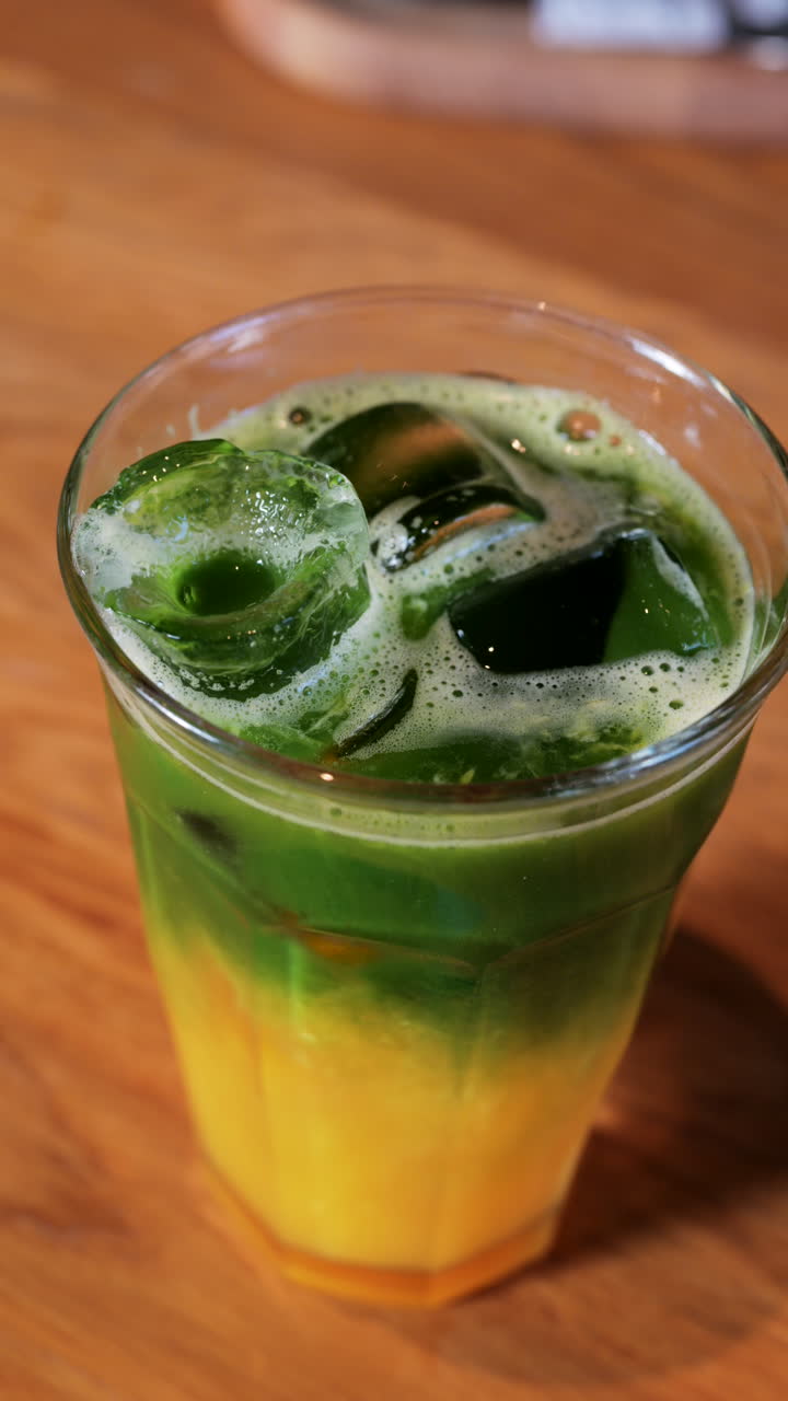 Close up of a glass of an iced orange juice matcha on a table at a cafe. Vertical