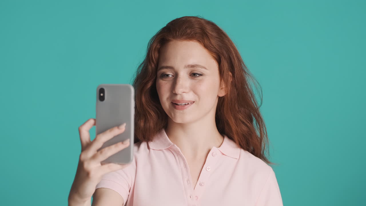 una chica pelirroja frente a la cámara sobre un fondo turquesa.