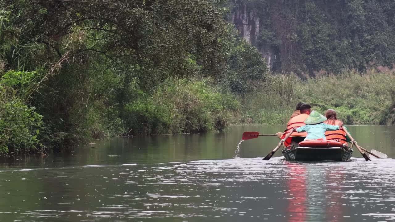 Due persone remano dolcemente lungo un fiume stretto, circondate da una vegetazione lussureggiante e acque calme