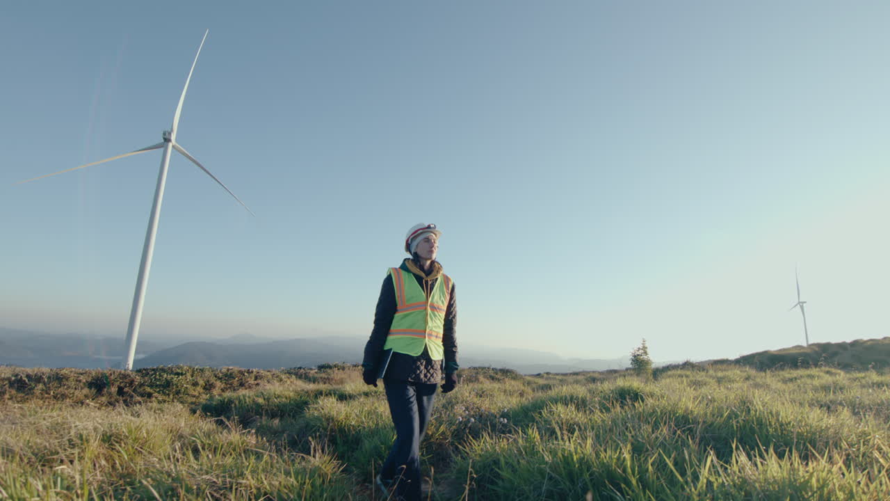 Female Engineer Walking with Tablet Through Wind Farm