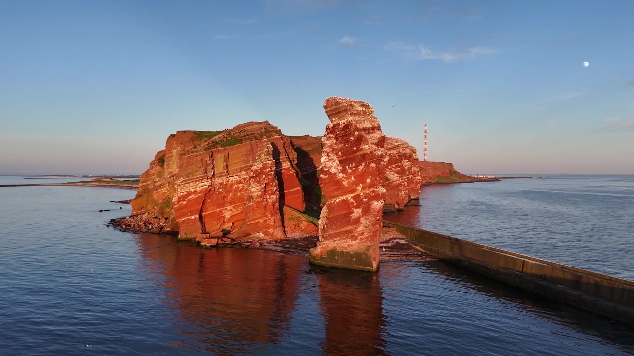 Seitliche Luftaufnahme der Langen Anna mit roten Sandsteinschatten, Vögeln und Brutklippen.