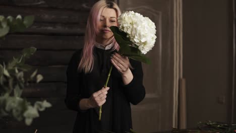 hermosa florista de cabello rosa con una flor de hortensia blanca gigante en las manos. se quita las hojas adicionales