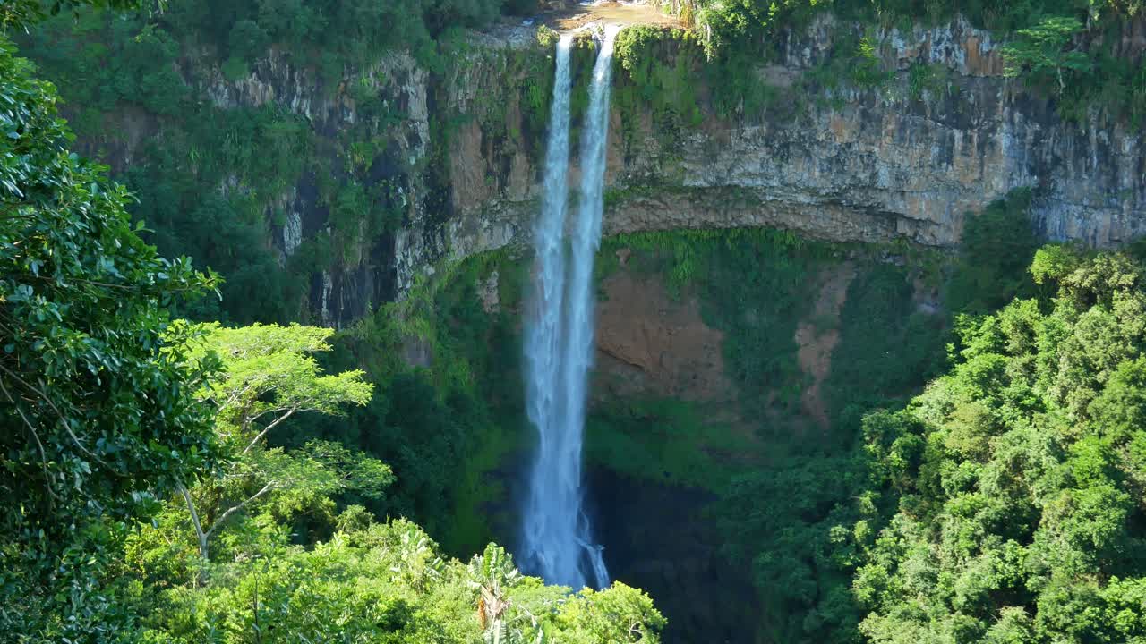 una toma de una cascada de chorro doble cayendo sobre una pared de roca natural, en un lugar muy frondoso