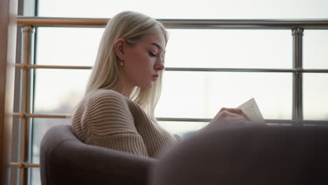 side view of student seated in mall reading her book, thoughtfully flipping through the pages, soft natural light coming through window, creating a calm and quiet atmosphere