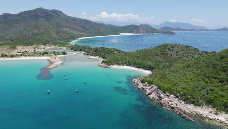 Rotating-aerial-over-crystal-clear-turquoise-waters-at-Binh-Tien-Beach-surrounded-by-green-cliffs-in-Vietnam