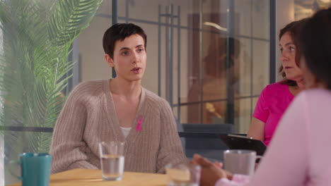 group of women wearing pink breast cancer awareness ribbons meeting and talking at therapy support group for cancer treatment patients 2