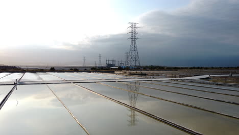 Close-up-of-salt-fields-with-pylons-and-wind-turbine-at-background