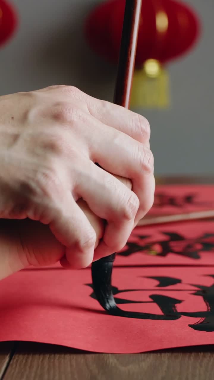 Vertical video: Touching brush tip painter's hands forming calligraphy on red paper for festival