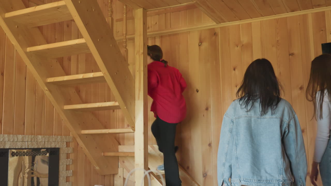 two friends return home and stand inside wooden cabin interior, wearing casual clothes and chatting while preparing to go upstairs, staircase and rustic wooden walls