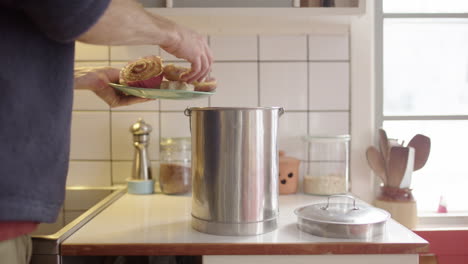 hombre descarga rosquillas rancias en un plato en un contenedor de compost de acero en la cocina