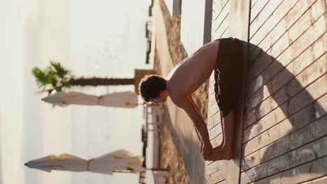 Vertical-video:-a-guy-in-black-shorts-doing-stretching-and-doing-yoga-on-a-sunny-beach