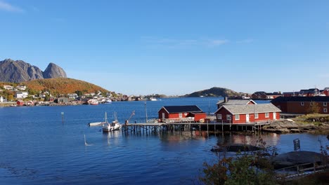 Calm-day-on-the-lofoten-islands,-beautiful-red-hut-with-a-boat-on-the-shore-of-a-deep-blue-bay