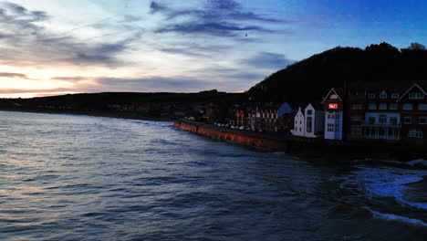 Sandsend-sea-front,-near-whitby,-drone-move-along-sea-wall-with-waves-breaking