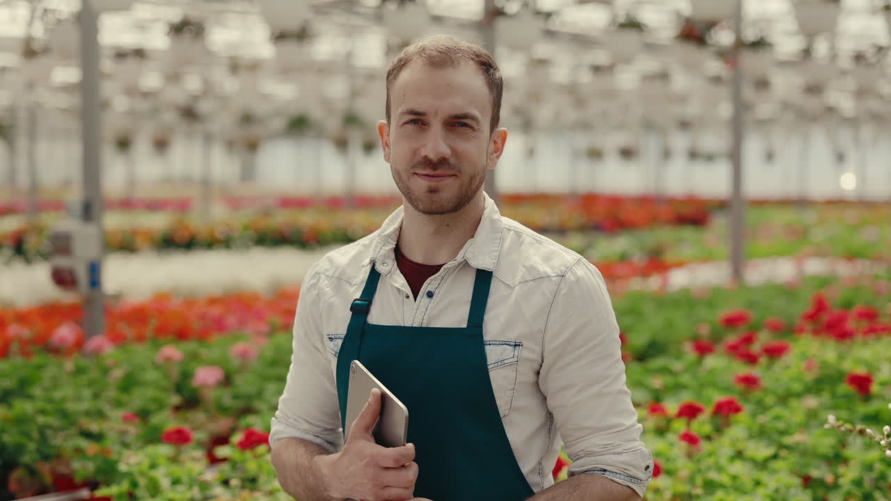 Gartner med tablet i et drivhus fyldt med blomster