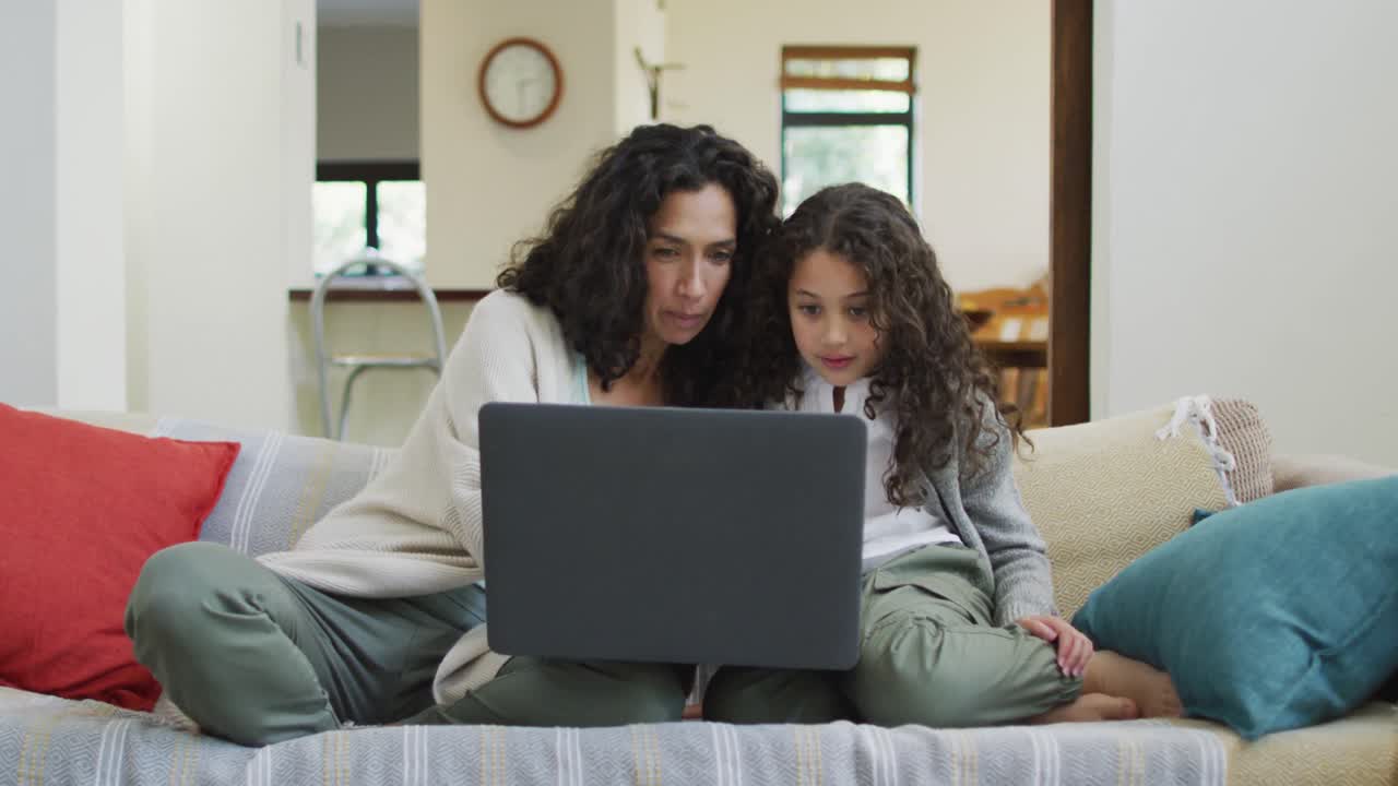 Happy mixed race mother and daughter sitting on the sofa,having fun and using laptop