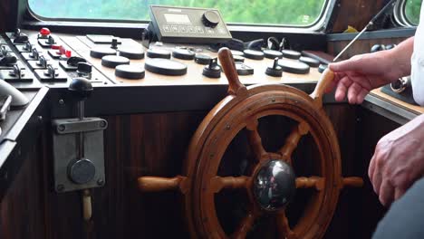 Hands-turning-old-fashioned-wooden-helmsman-wheel-on-a-boat---Handheld-closeup-of-Wheel-inside-wheelhouse