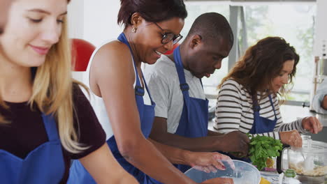 Male-And-Female-Adult-Students-Preparing-Ingredients-For-Dish-In-Kitchen-Cookery-Class