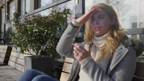 mujer joven tomando café afuera bajo el sol de la mañana, usa la mano para proteger los ojos