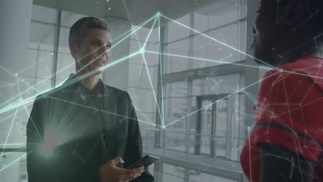animation of network of connections against two diverse businesswomen discussing at office