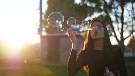 Verträumte-Hispanische-Frau,-Die-Bei-Sonnenuntergang-Verträumte-Seifenblasen-Im-Freien-Mit-Sonnenschein-Und-Blendenflecken-In-Zeitlupe-Bläst