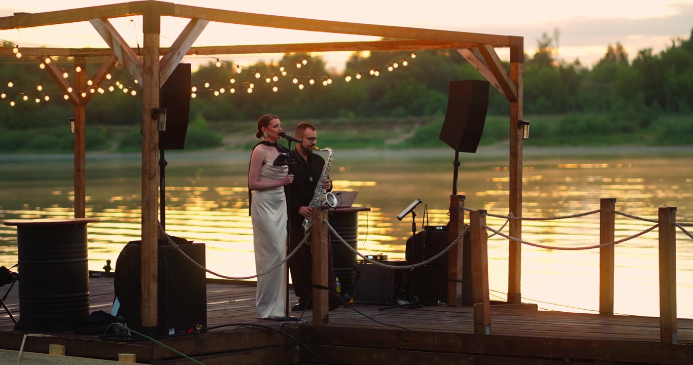 Female Singer and Saxophonist Performing on a Riverside Pier at Sunset