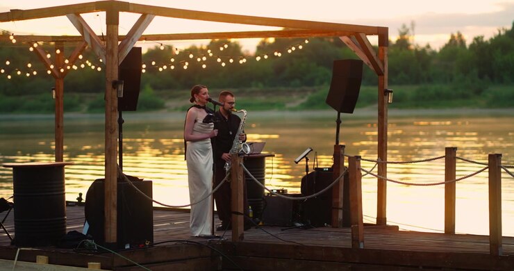 Female Singer and Saxophonist Performing on a Riverside Pier at Sunset