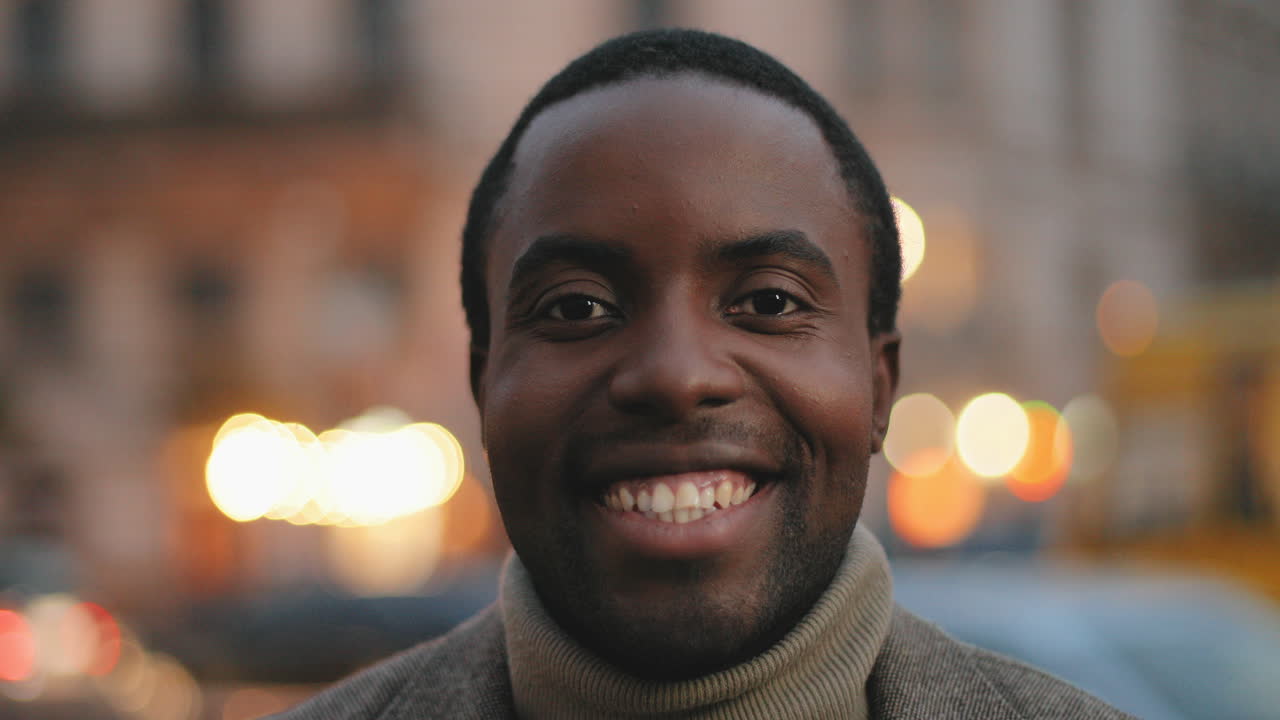 Close-up view of African American young man looking and smiling to the camera in the street in the evening