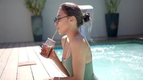 relaxing by pool, woman in swimsuit drinking iced tea with straw