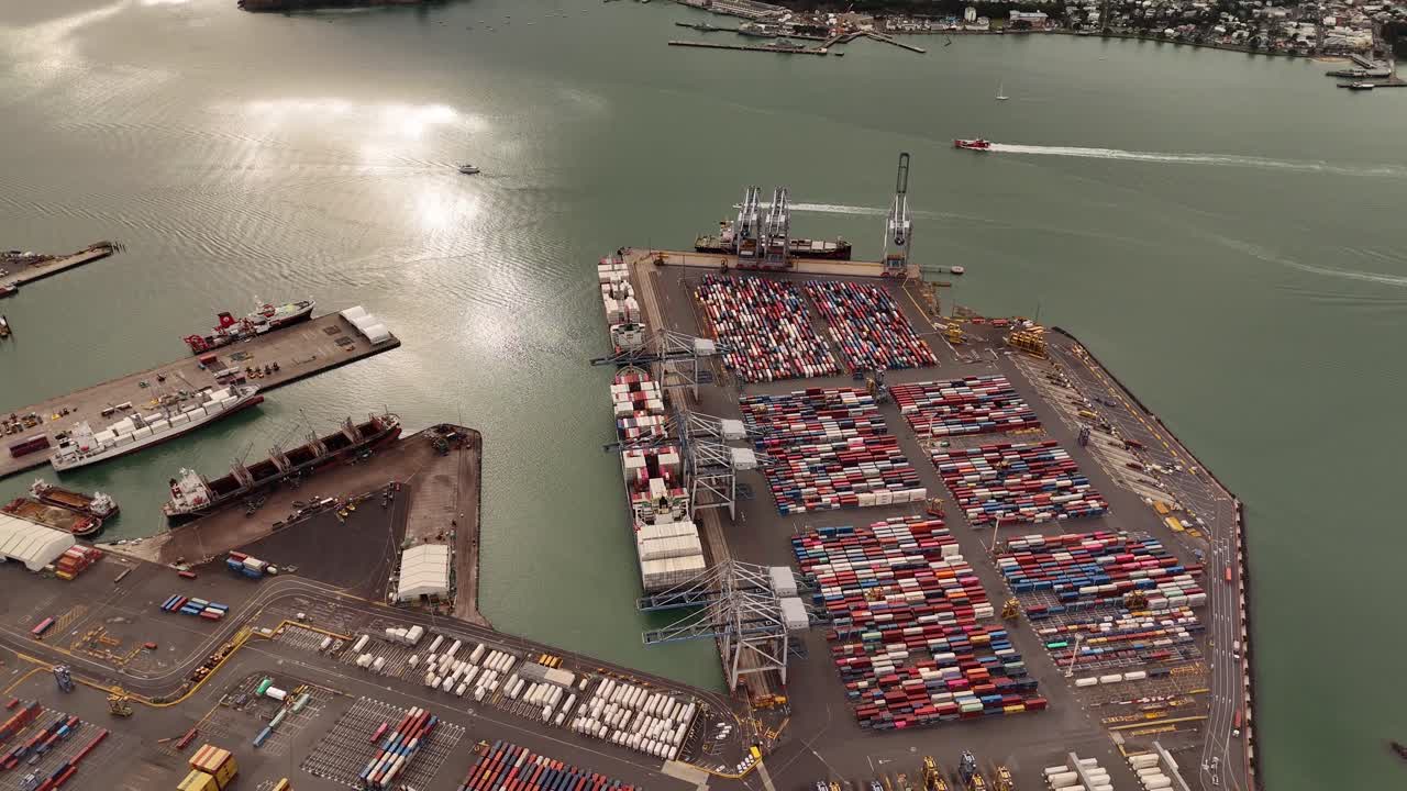 A smooth 4K 60fps drone shot flying backward over stacks of colorful cargo containers at the Port of Auckland, revealing the immense scale of the industrial area. Perfect for logistics or trade themes
