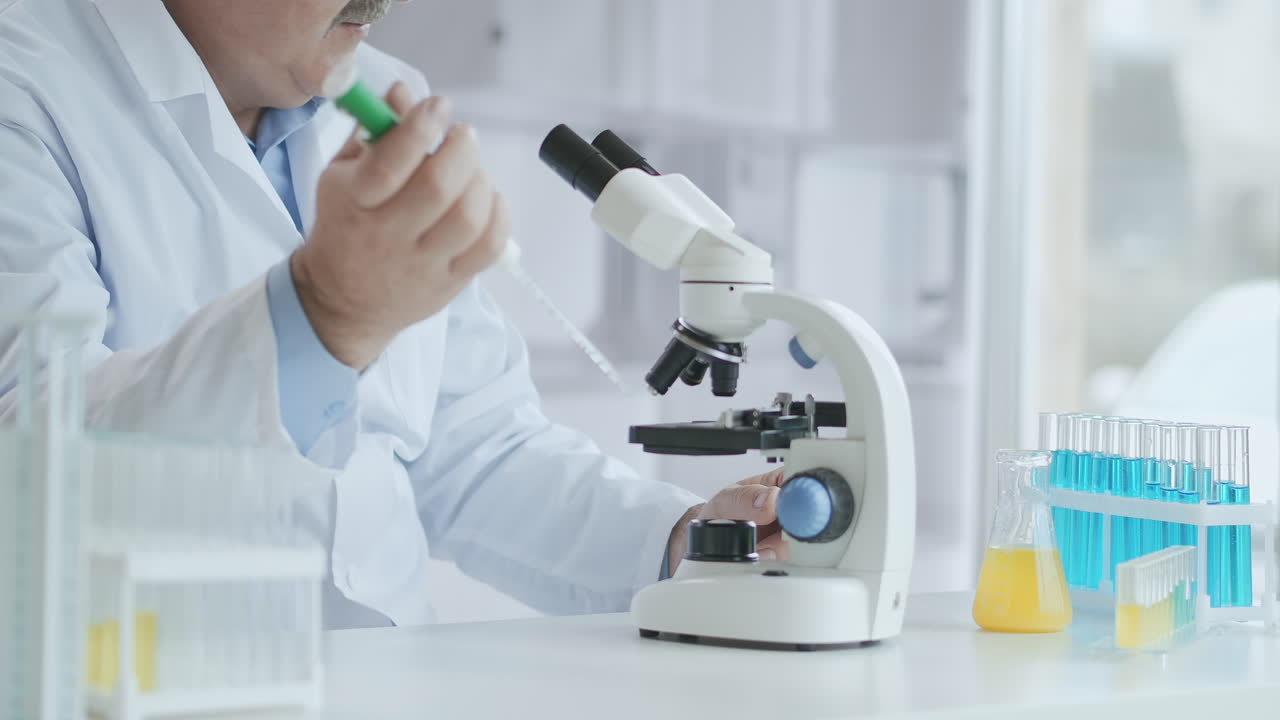 Bearded Caucasian male researcher wearing protective glasses and working with a microscope spbas. scientist using microscope in a laboratory. Search for coronavirus vaccine. High quality 4k footage