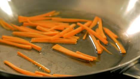 cooking carrots for asian food in a steel pan, handheld close up shot