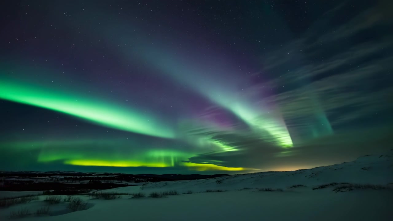 Brillanti tende aurorali verdi e verde acqua si estendono attraverso il cielo notturno blu scuro sopra colline ondulate coperte di neve, con visibili cambiamenti nell'altezza della banda, nel bagliore e nell'intensità attraverso un paesaggio invernale remoto.