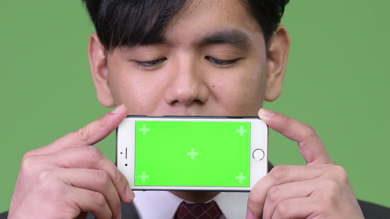 젊은 잘생긴 아시아 사업가 휴대전화를 보여줍니다.