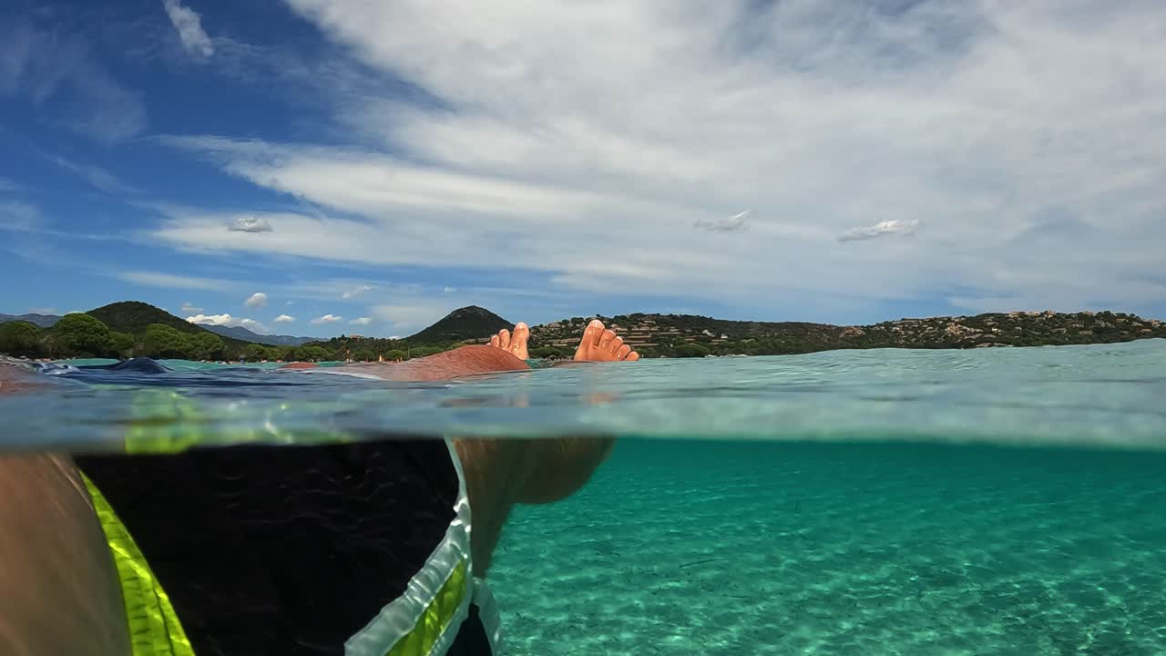 프랑스 코르시카 섬의 산타 줄리아 유명한 해변에서 바닷물에 떠 있는 동안 편안한 남자 다리와 발의 1인칭 낮은 각도 pov