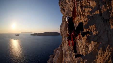person rock climbing on a cliff overlooking the ocean at sunset