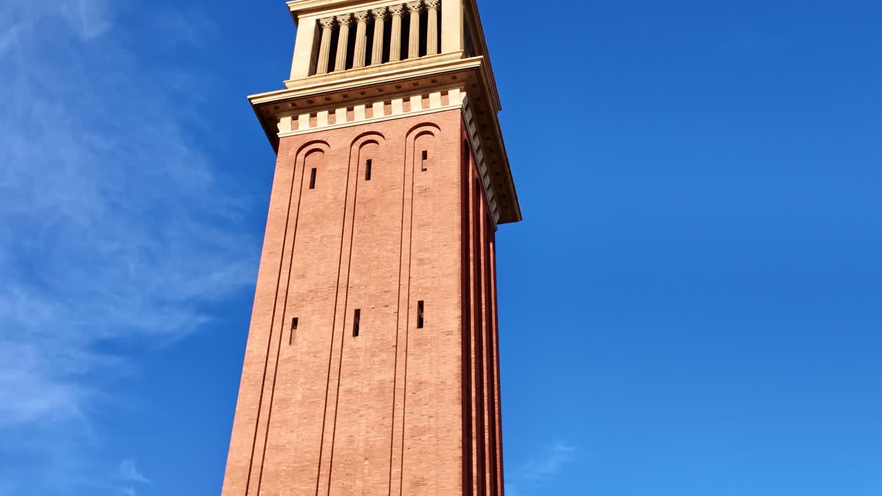 Torre Veneziana a Plaça Espanya a Barcellona, Catalogna, Spagna, caratterizzata da una struttura alta in mattoni con dettagli classici e sfondo di cielo azzurro limpido, un punto di riferimento iconico, carrellata verso l'alto, rivelazione con panoramica verticale.