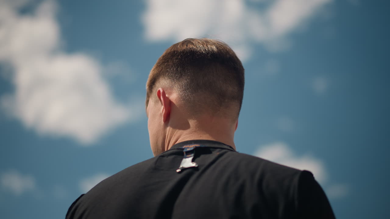 운동을 준비하며 운동복을 입는 남성, 야외 운동 세션 전에 어두운 상의를 입는 개인, 하늘색과 활기찬 분위기 속에서 남성이 밖에서 검은색 셔츠를 정리해요.