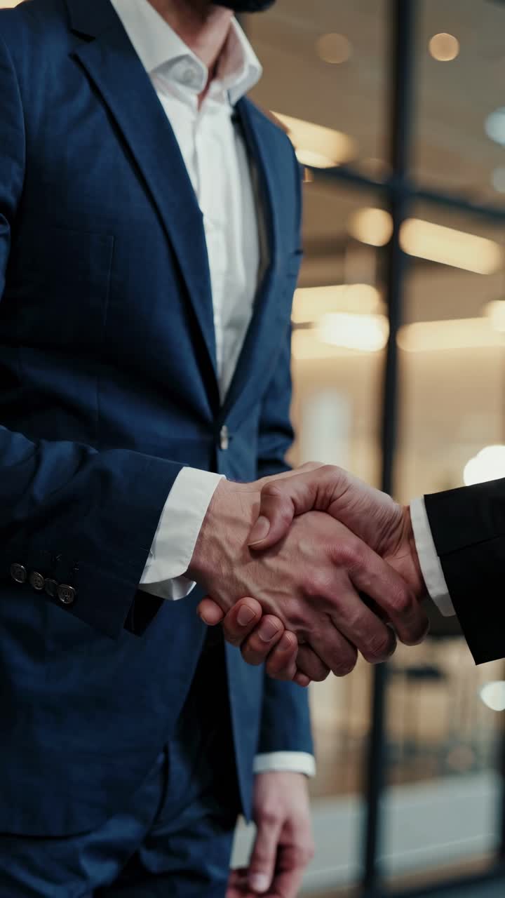 Video ravvicinato di due uomini d'affari che si stringono la mano in un ufficio moderno, ripreso da una angolazione bassa.