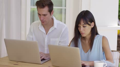 Young-couple-sitting-at-table-using-laptop