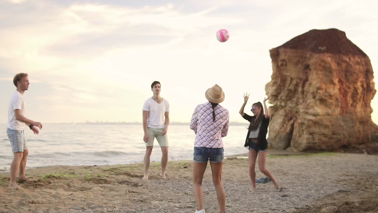 jóvenes amigos alegres jugando al voleibol en la playa junto al mar por la noche. vacaciones activas. disparo en cámara lenta