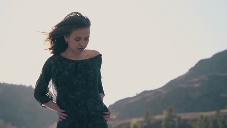 검은 드레스를 입은 짧은 머리카락의 소녀가 산을 반대하여 포즈를 취합니다.