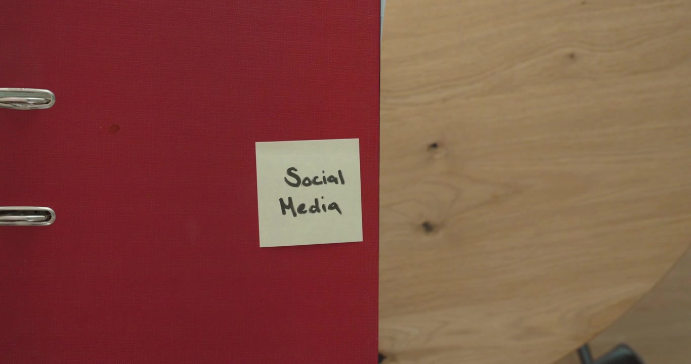 Uma mão pega um smartphone de uma mesa e o coloca de volta ao lado de um post-it com a etiqueta "Mídias Sociais". Conceito de hábitos de smartphone, distração digital e tempo de tela