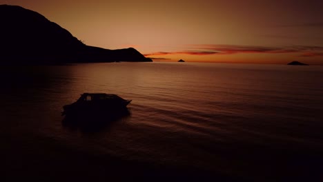 Slow-aerial-shot-of-a-dark-orange-sunset-at-dusk-with-a-boat-on-Lake-Titicaca-in-Peru