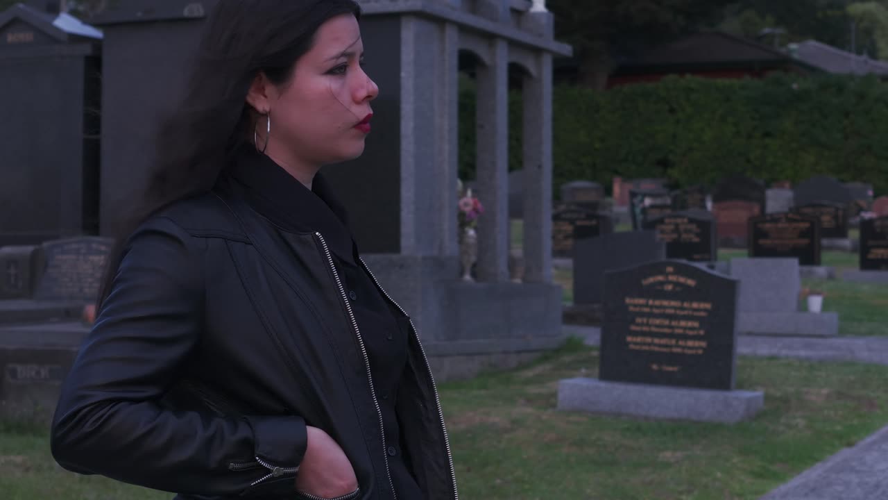 Jovem mulher permanece pensativa entre lápides ao crepúsculo no cemitério de Melbourne. A imagem captura o ambiente tranquilo e reflexivo sob a suave luz do entardecer num cenário sereno.