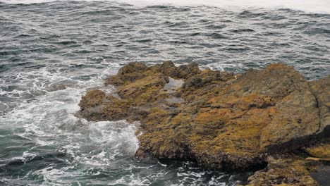 Slow-motion,-medium-shot-of-ocean-waves-crashing-on-rocking-shore