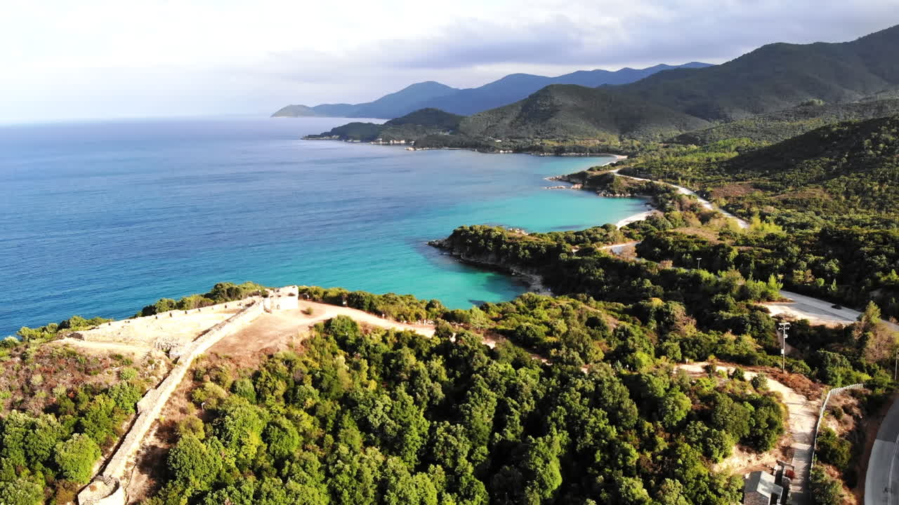 Colline ricoperte di una vegetazione lussureggiante. Resti di antiche strutture sulla cima della collina. Costa del Mar Egeo. Strada con auto in movimento. Grecia